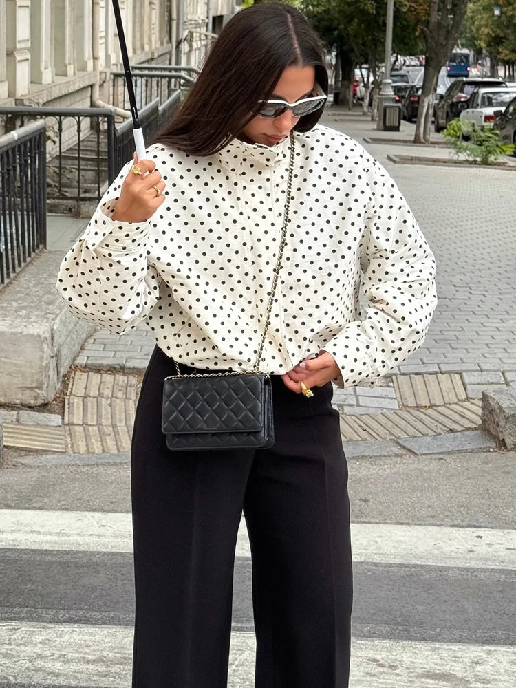 Woman in polka dot coat holding a black bag outdoors.