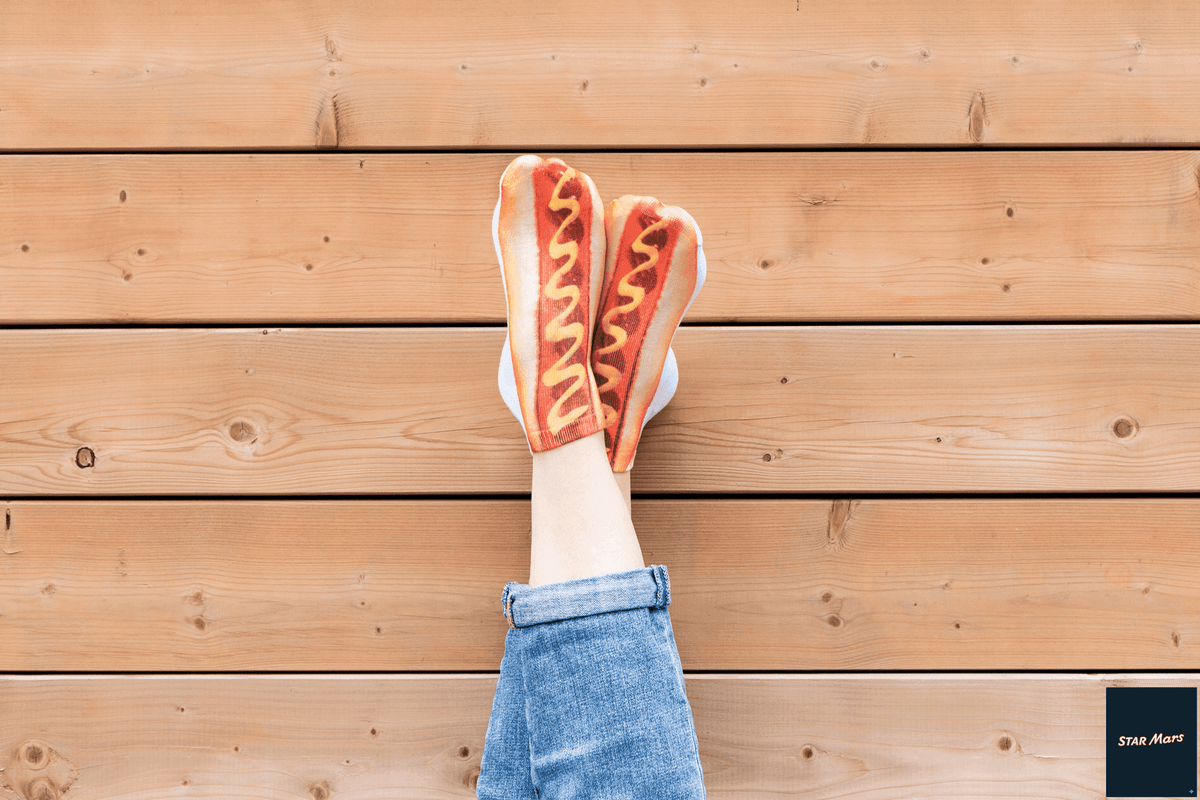 Person wearing red and yellow hotdog socks with mustard detail, paired with blue jeans against wooden deck background.