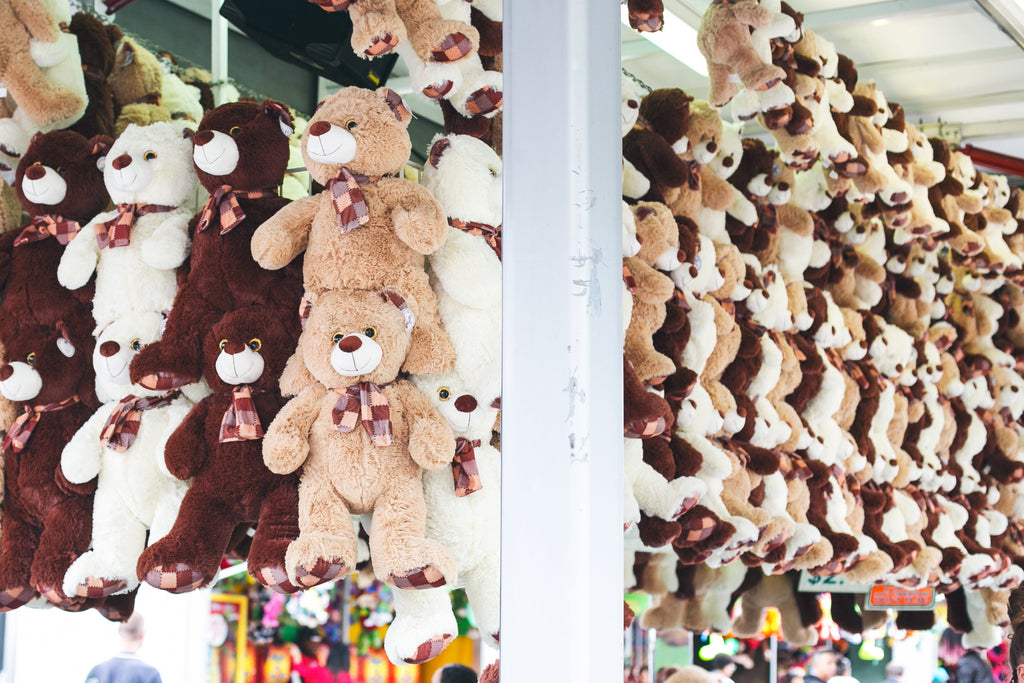 # Alt Text

Colorful Baby Alien Plushies hanging in rows at a carnival game booth, featuring brown, white, and tan fuzzy toys with plaid ribbons.